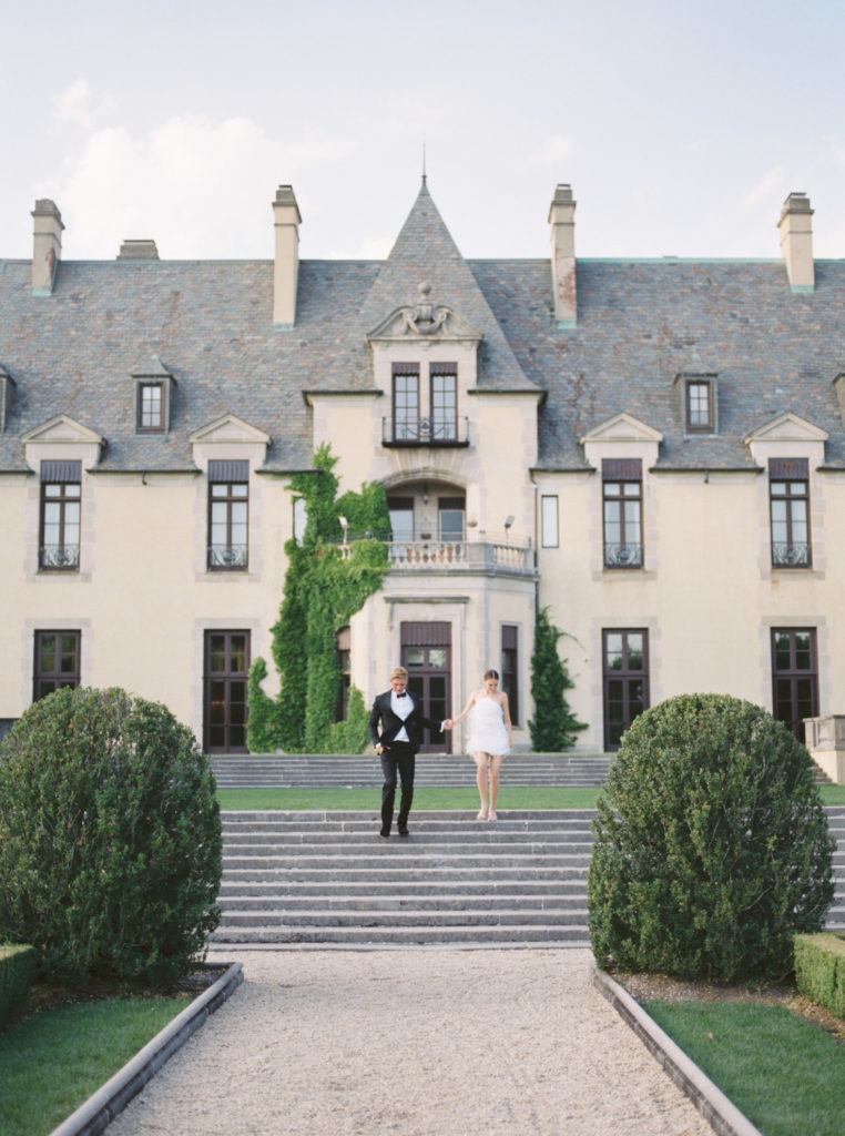 front view of Oheka Castle with bride and groom walking down the stairs together