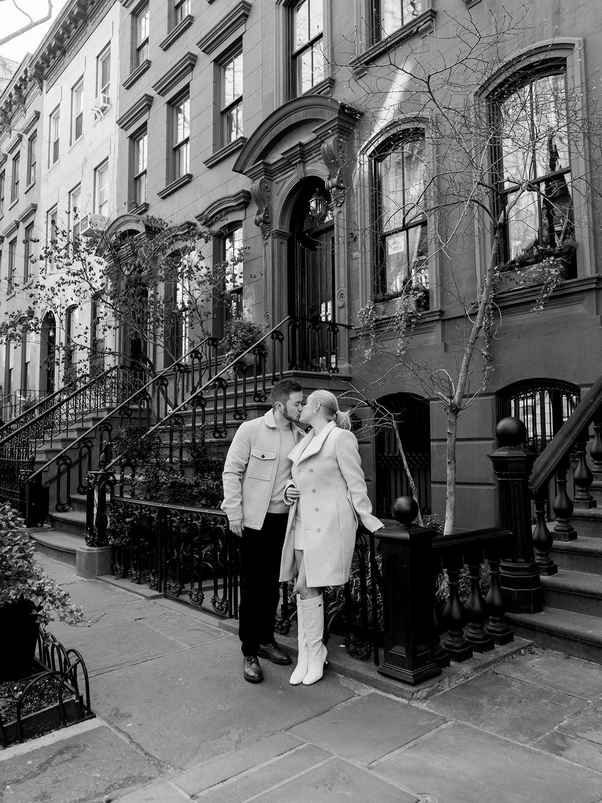 A couple kissing on the west side leaning against a fence in front of the brown stones.