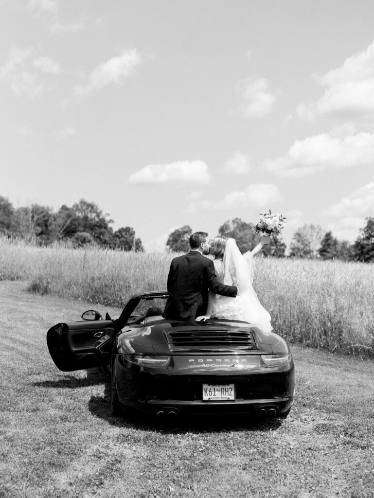 bride and groom sitting on the convertible kissing