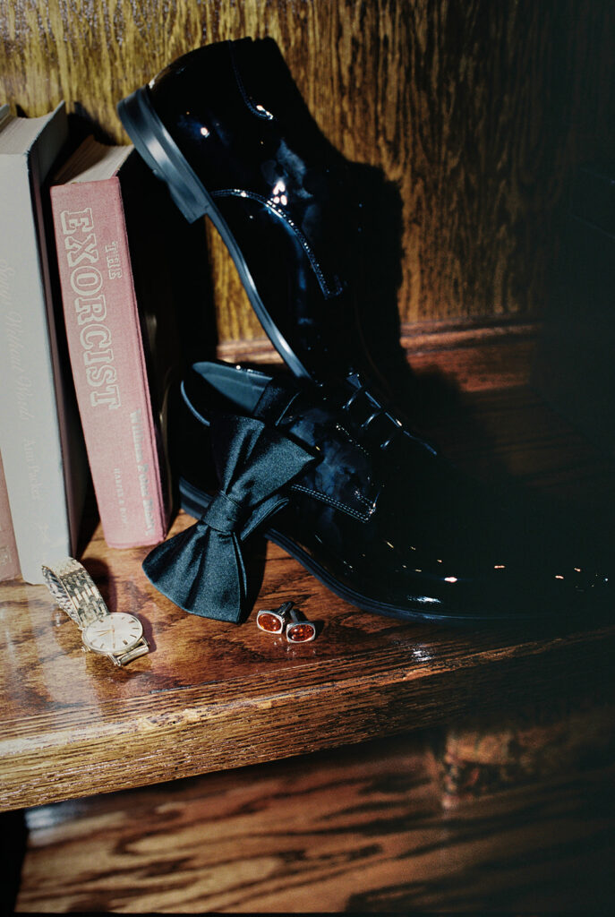 Photograph of the groom's shoes in the bookcase with his cufflinks and bow tie on film with direct flash for this wedding detail trends.