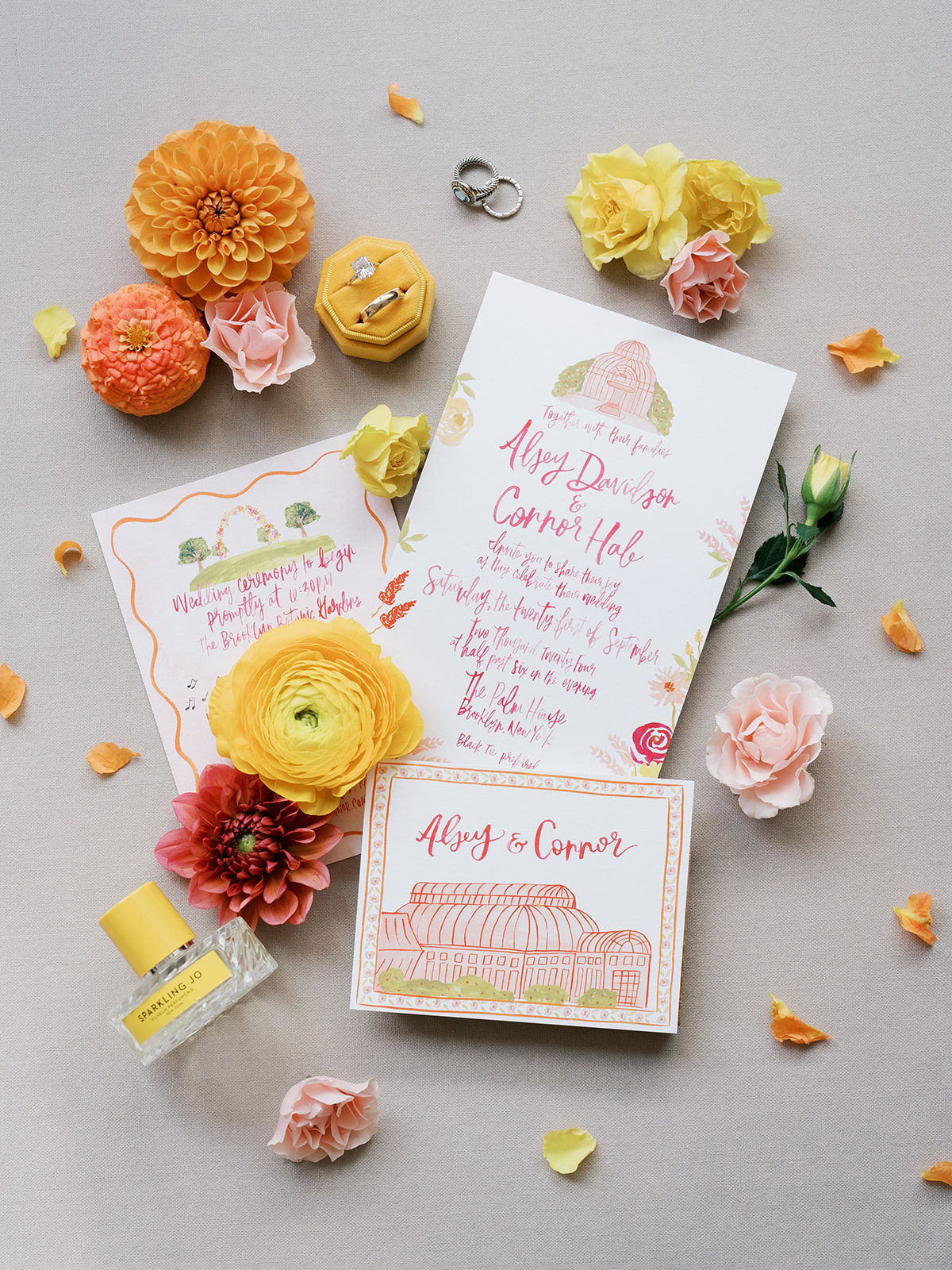 Stationery flat lay of a wedding with paper, florals, and perfume laid out in a scattered way.