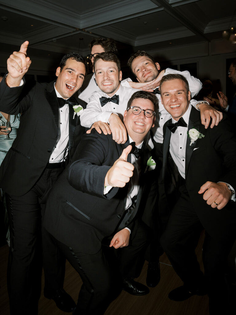 The groom and groomsmen on the dance floor stopping for a picture.