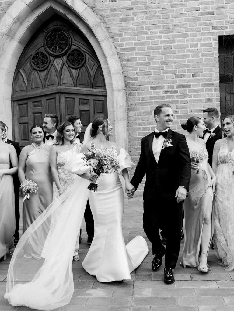 Full wedding party walking towards the camera in a documentary style image in black and white.