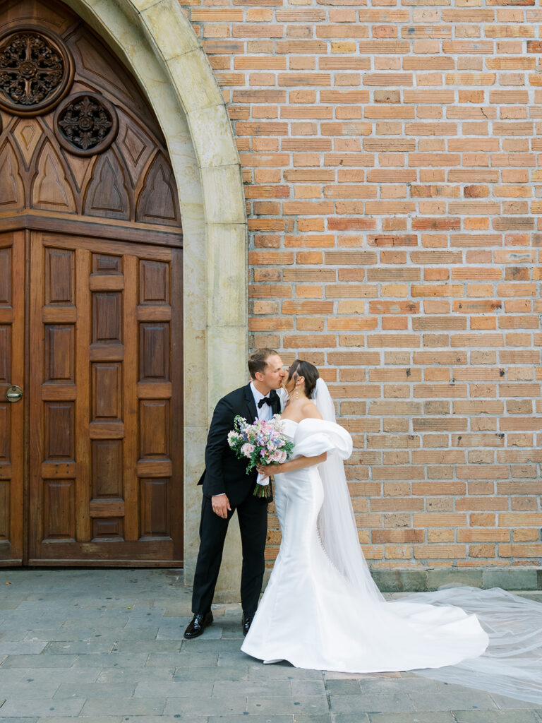 Bride and groom portrait in front of the church door. They are kissing.