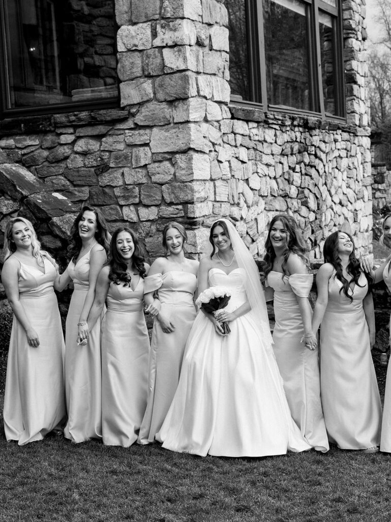 The bride surrounded by her bridesmaids for a portrait while they are laughing together.
