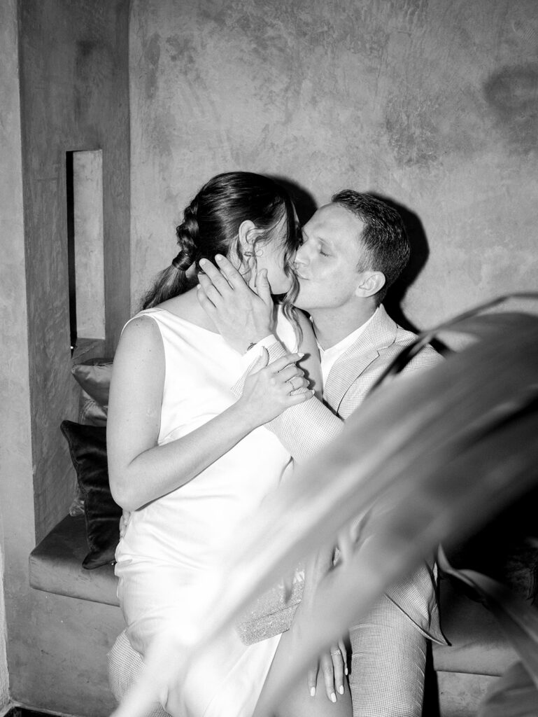 A black and white image of the bride and groom kissing. His hand is on her face.