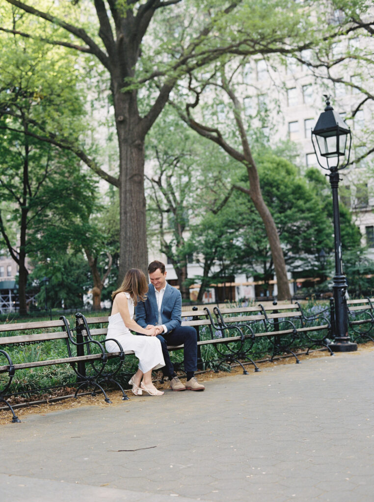 The couple sitting together holding hands on a bench looking down at their hands.