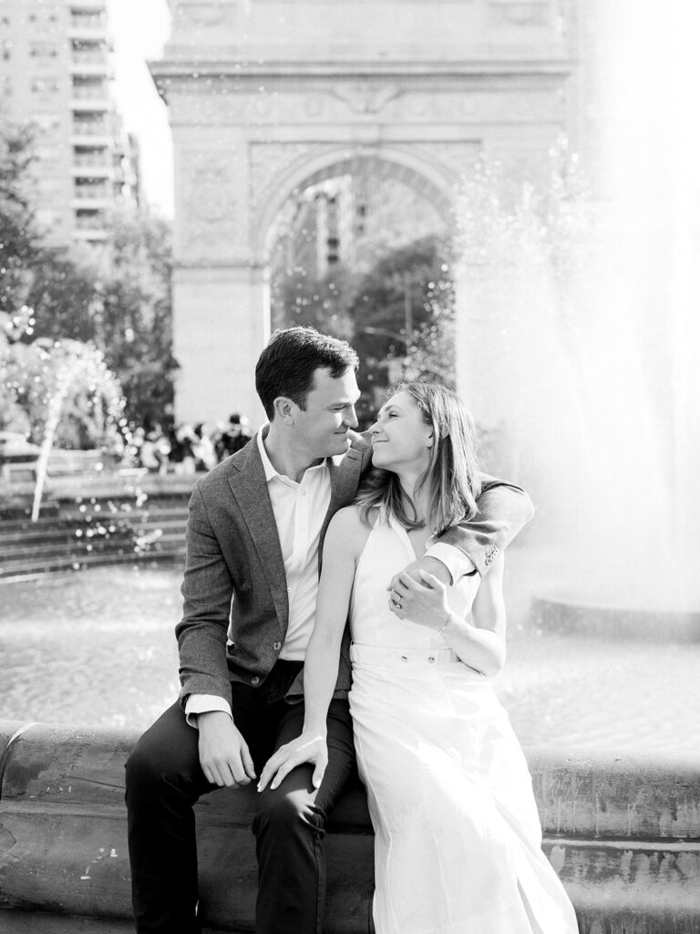 Black and white image of the couple sitting on the fountain at their Greenwich Village Engagement Session