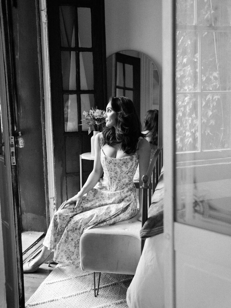 The bride to be seated on a bench in the guest room looking out the window.