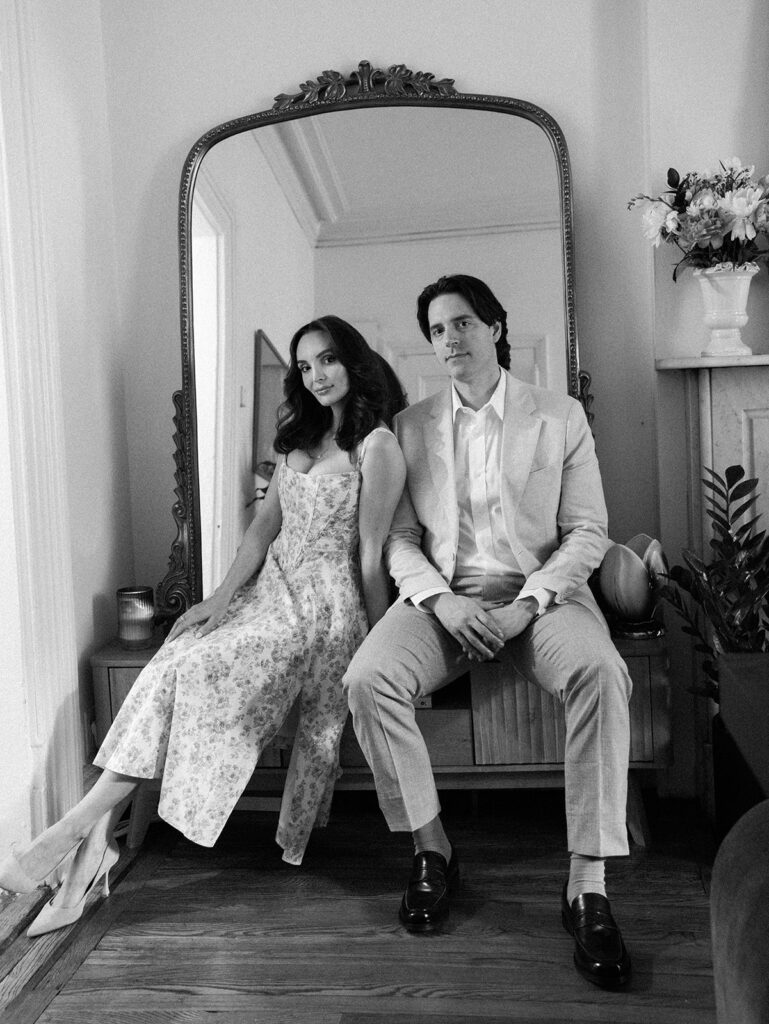 The couple looking at the camera while sitting on a bench in their home.