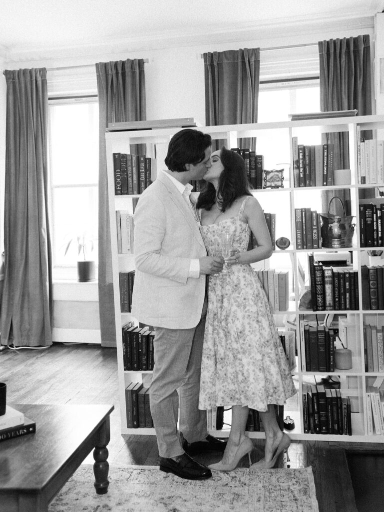 The couple kissing in front of the bookcase in their living room during their West Village engagement photos.