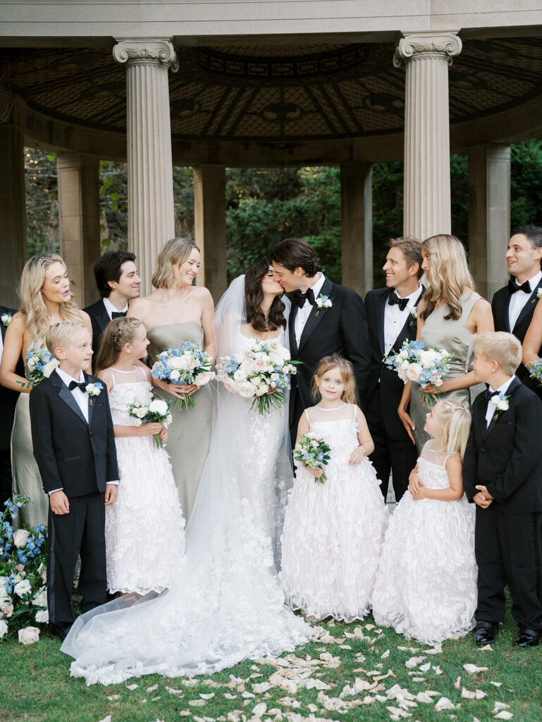 The wedding party with the bride and groom kissing in the middle.