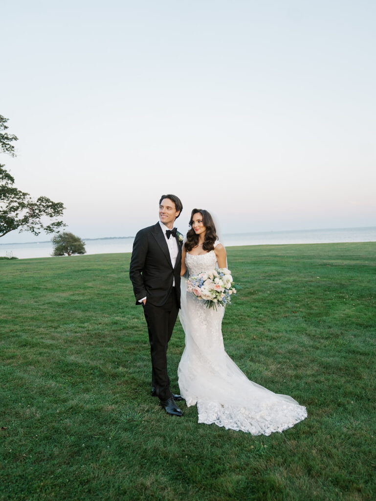 Bride and groom posing for a portrait in the field with the water in the background.