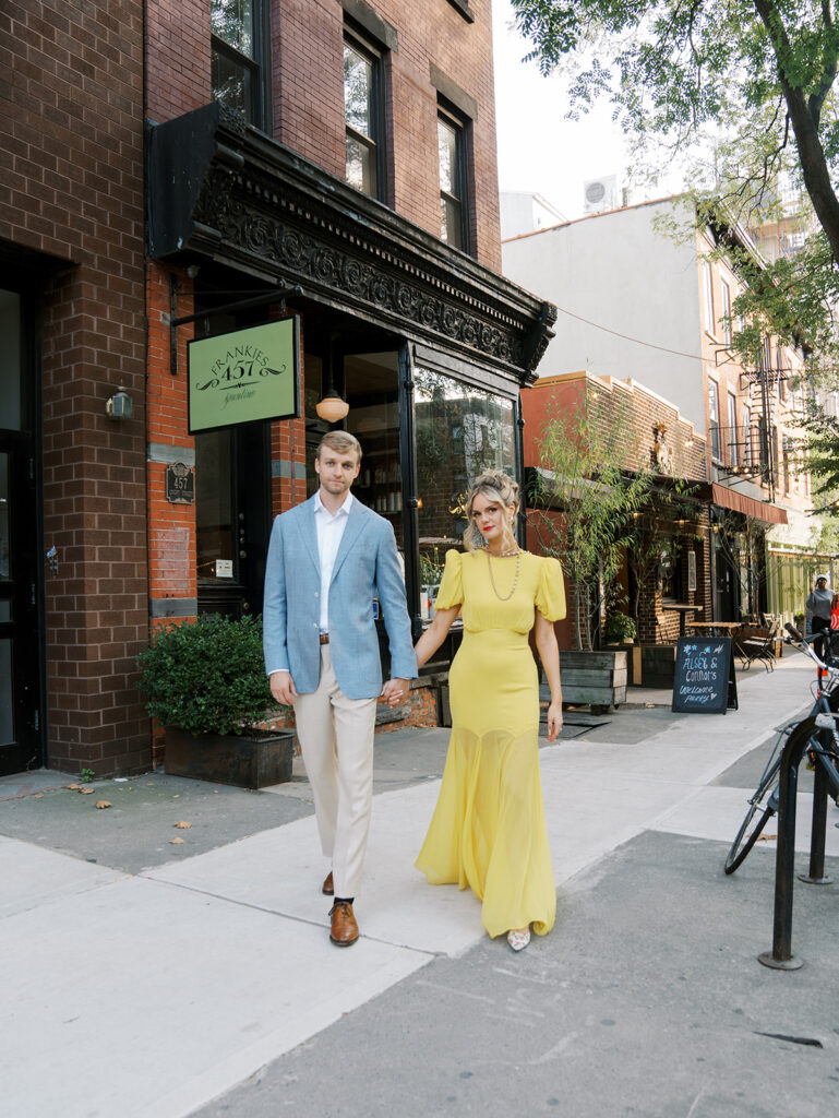 The bride and groom holding hands looking at the camera outside of Frankie's Spuntino.