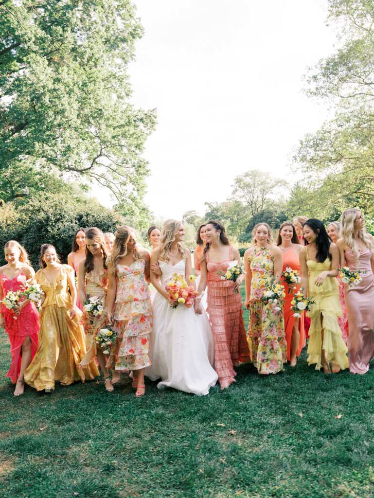 The bride and her bridesmaids walking together in the gardens looking and laughing at each other.