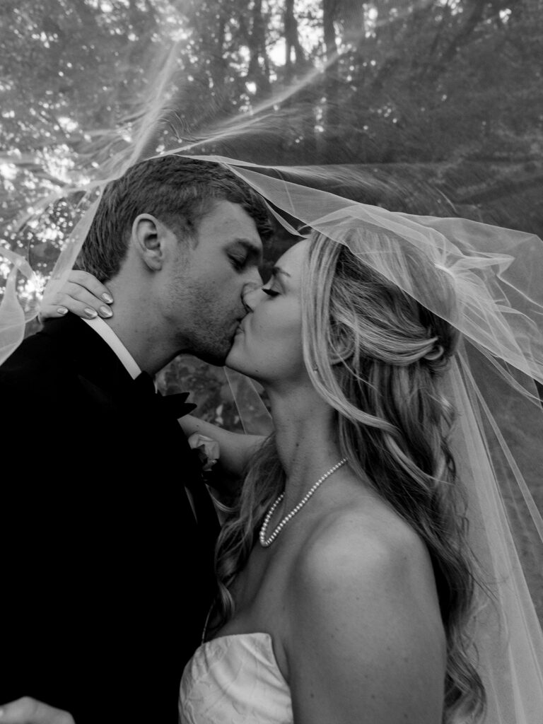 The bride and groom kissing under the veil in black and white.