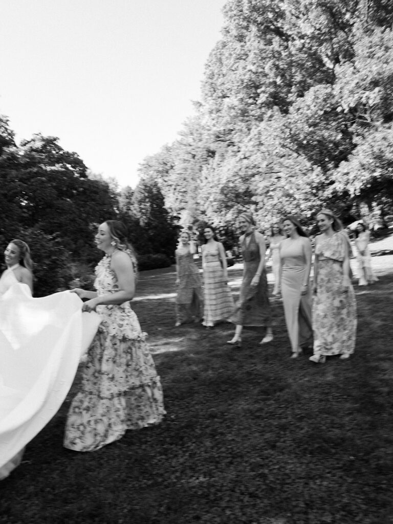 Bridesmaids walking behind bride in black and white.