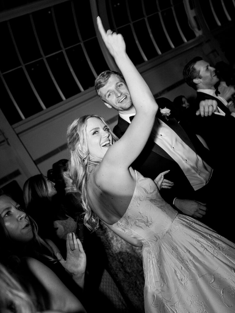 Bride and groom on the dance floor. Bride has her hand in the air looking over her shoulder.