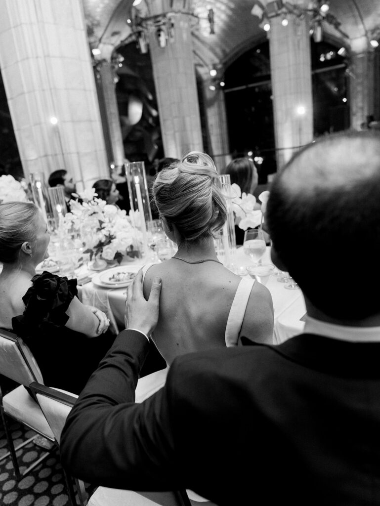 A view of the groom gently touching the shoulder of the bride during speeches.