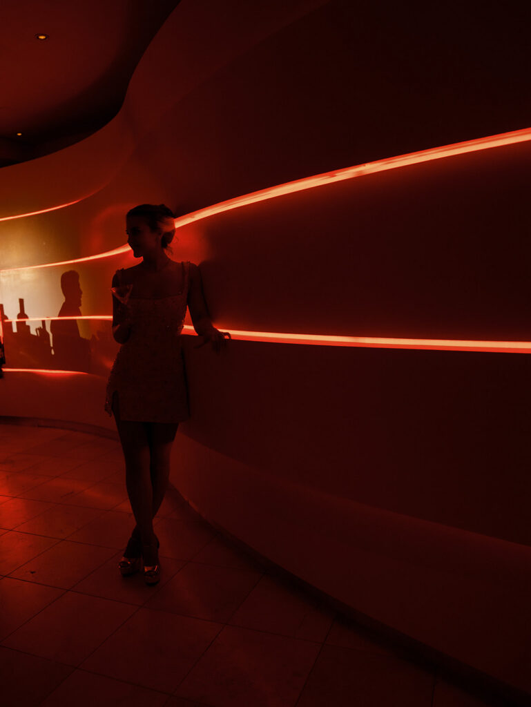 A portrait of the bride at her after party against a red lit wall.