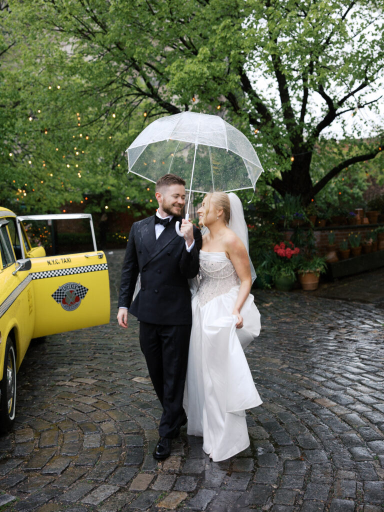 The bride and groom walking together looking at each other under the umbrella at their rainy River Cafe wedding.