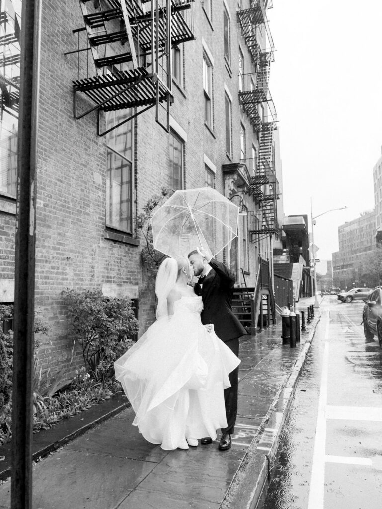 Bride and groom sharing a stolen kiss while walking along the street sidewalk in the rain.