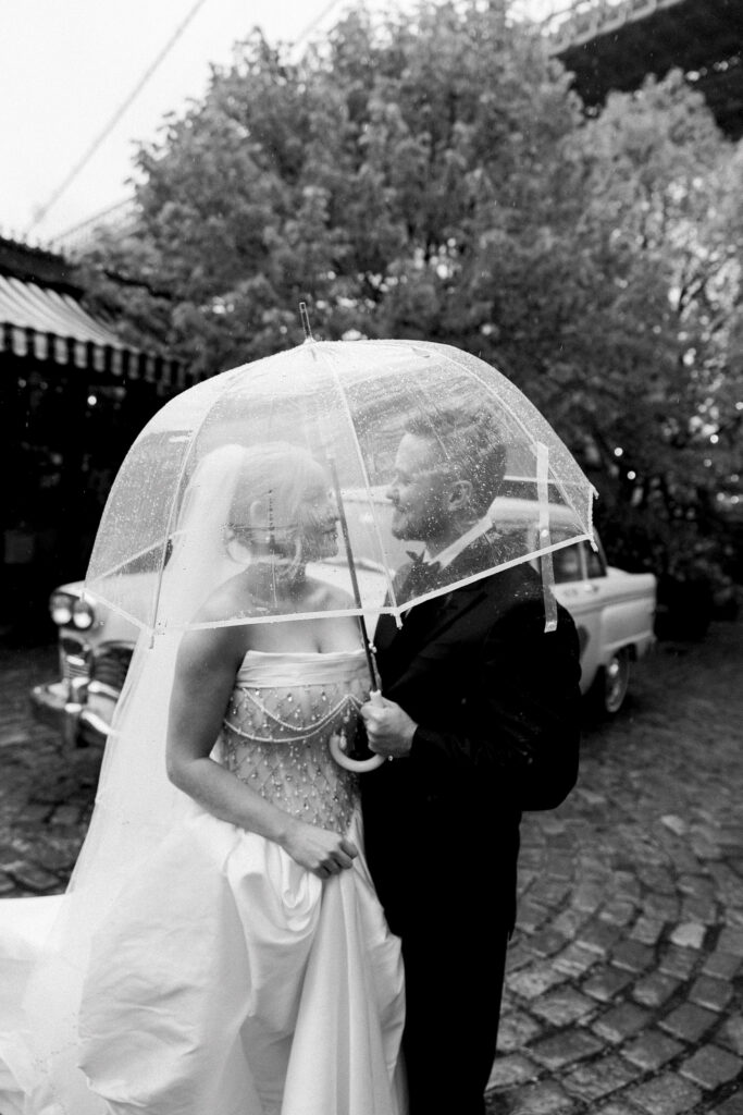 Bride and groom longingly looking at each other under the umbrella at their rainy river cafe wedding.