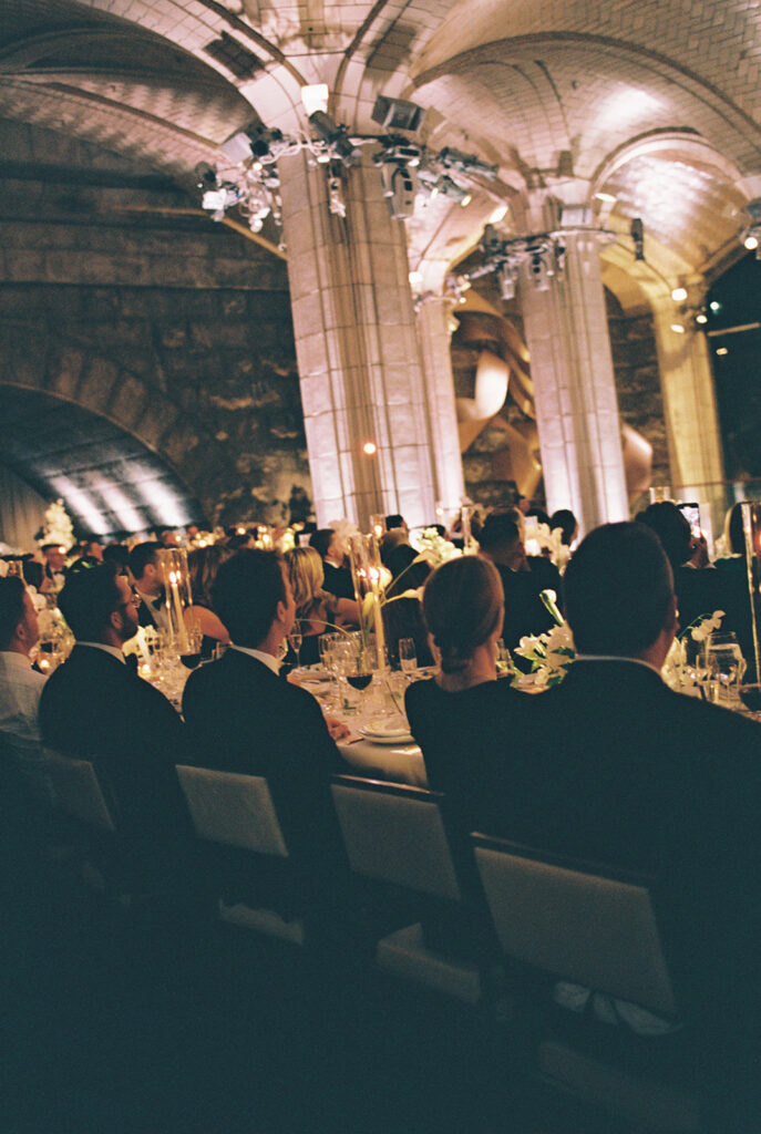 This is a picture of the guests at a wedding reception listening to speeches from the rear view.