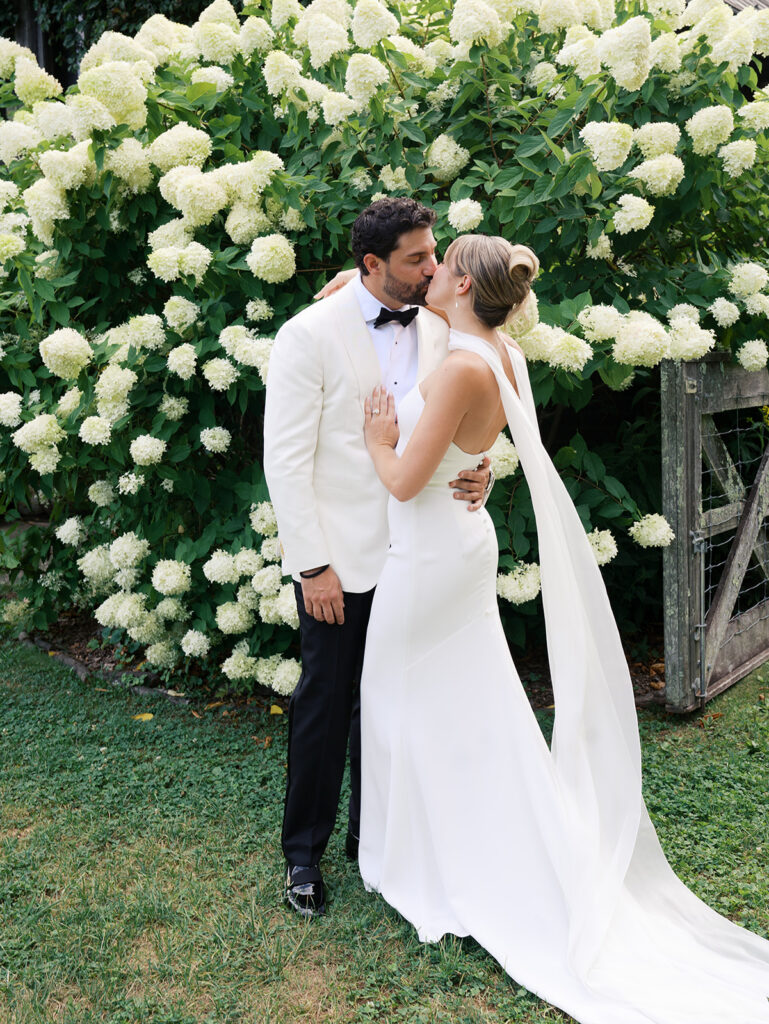 The bride and groom kiss in front of a large hydrangea bush at their Blue Hill at Stone Barns Wedding.