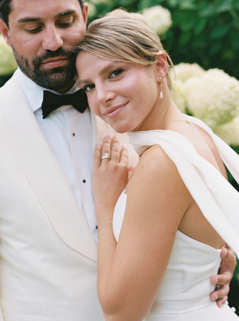 The bride snuggling into the groom and looking at the camera.