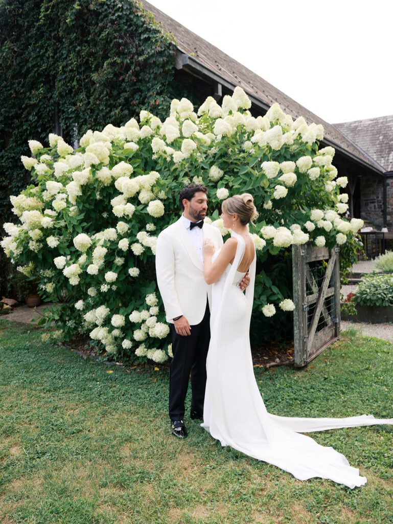 A pulled back view of the bride and groom against the hydrangea bush.