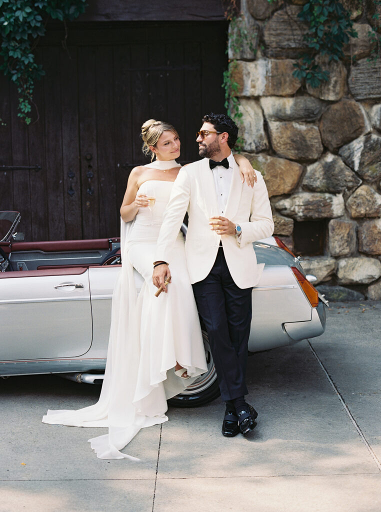 The bride and groom sitting on the car enjoying a cocktail and a cigar at their Blue Hill at Stone Barns Wedding.