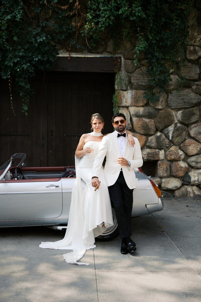 A pulled back view of the bride and groom against the car.