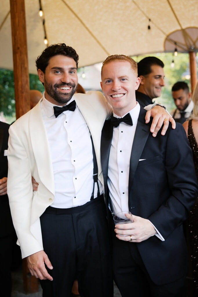 The groom with a friend posing for a portrait at cocktail hour under the tent.