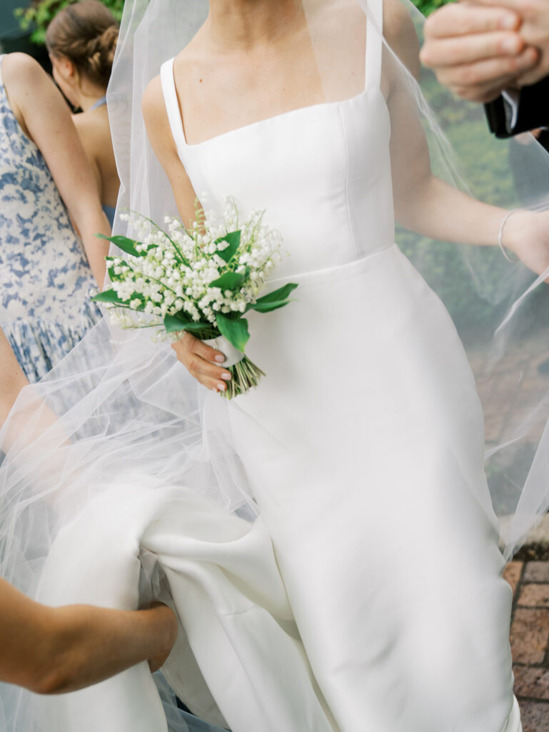 A close up of the bride adjusting her veil with a midcrop of her midsection.