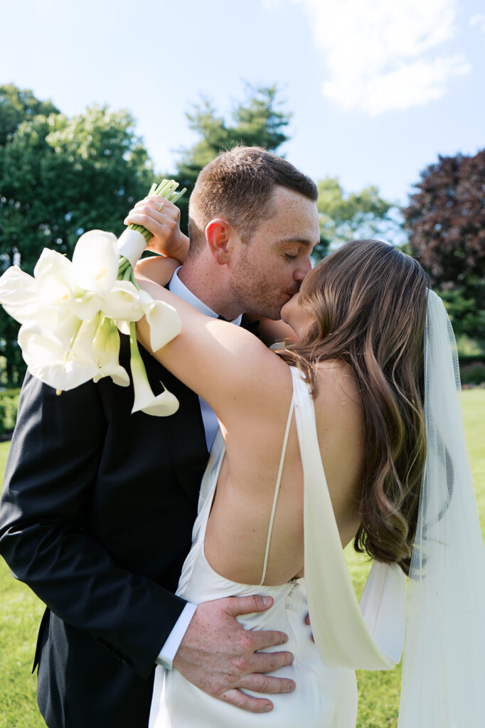 Bride and groom wrapped in a hug kissing with the flowers around his neck asking how many hours of wedding coverage do I need?